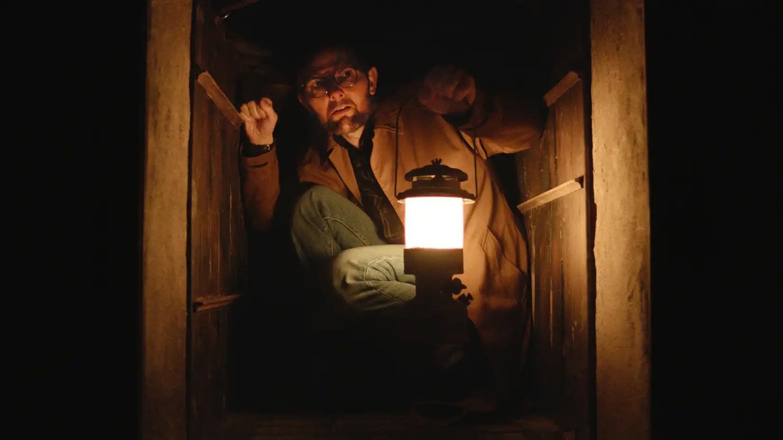 Ohm (Adam Scott) holds a lantern in a tightly enclosed space in Hokum
